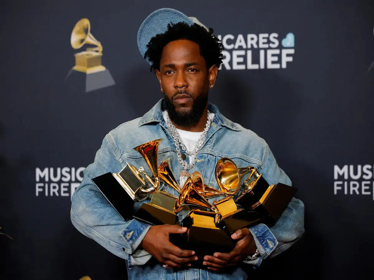 Kendrick Lamar holding a nomination placard in front of the AMA step-and-repeat backdrop